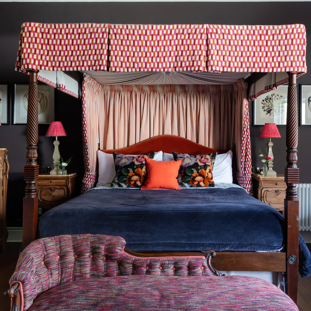 A richly decorated bedroom at the Cromlix Hotel featuring a grand four-poster bed with patterned drapes and canopy, a dark blue velvet bedspread, floral and orange pillows, bedside tables with red lamps, and a patterned chaise lounge in the foreground.